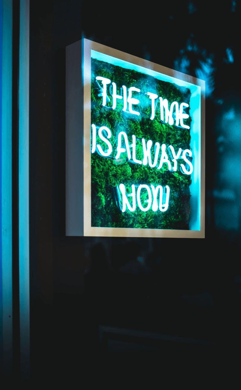Photo with text in neon 'The time is always now'. The photo is the image that belongs to the intro of the themes of Business Design Agency.