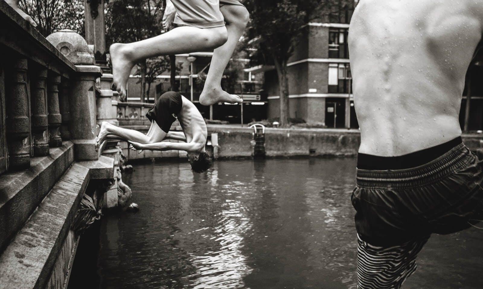 Boys jumping in city canal in black and white 